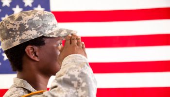 African descent military woman salutes American flag.