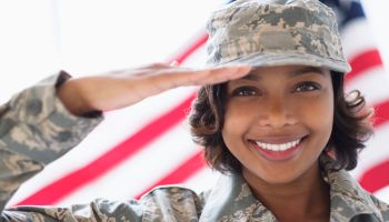 Portrait of smiling Mixed Race soldier saluting near American flag