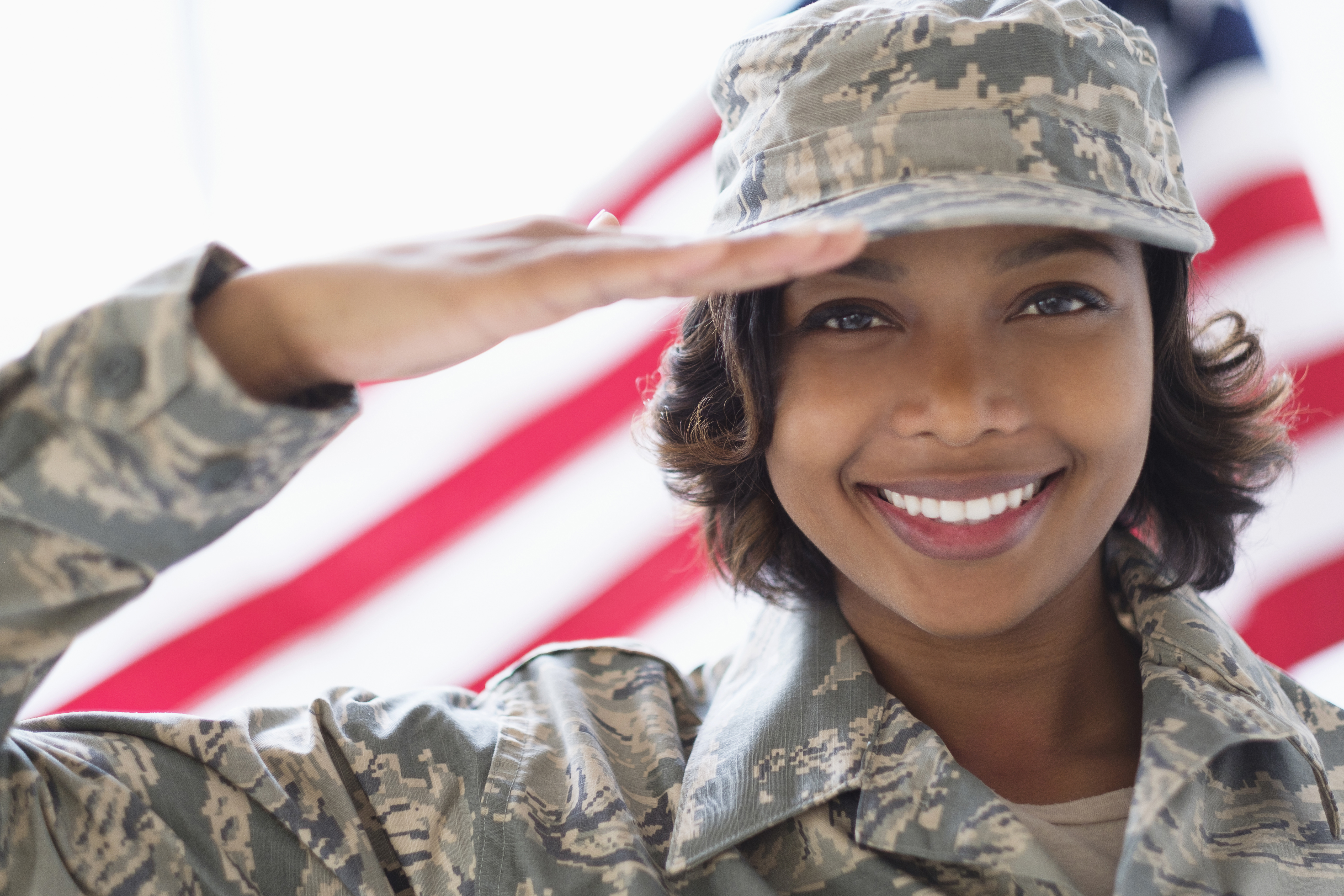 Portrait of smiling Mixed Race soldier saluting near American flag