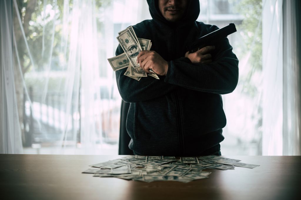 Smiling Mid Adult Businessman Holding Money And Gun While Standing In Office