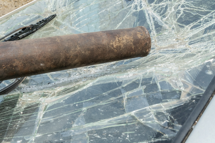 The iron pipe lies on the broken windshield of the car. Damage to the windshield with the power of an iron pipe, glass in cracks