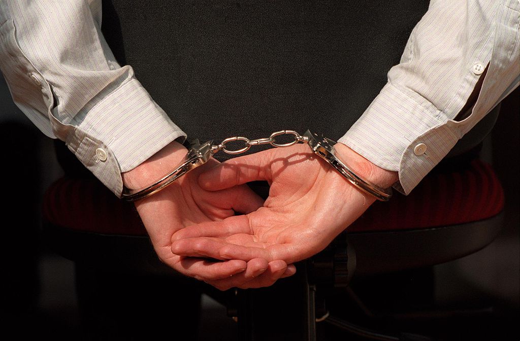 The picture shows hands handcuffed together. The person is wearing a business sh