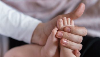 Female hands holding the little legs of a newborn baby.