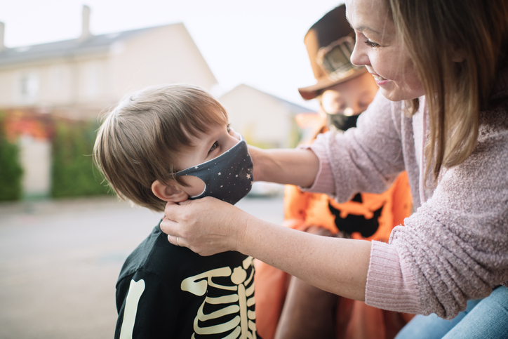 Mother putting protective face mask on her child during COVID-19 pandemic on Halloween