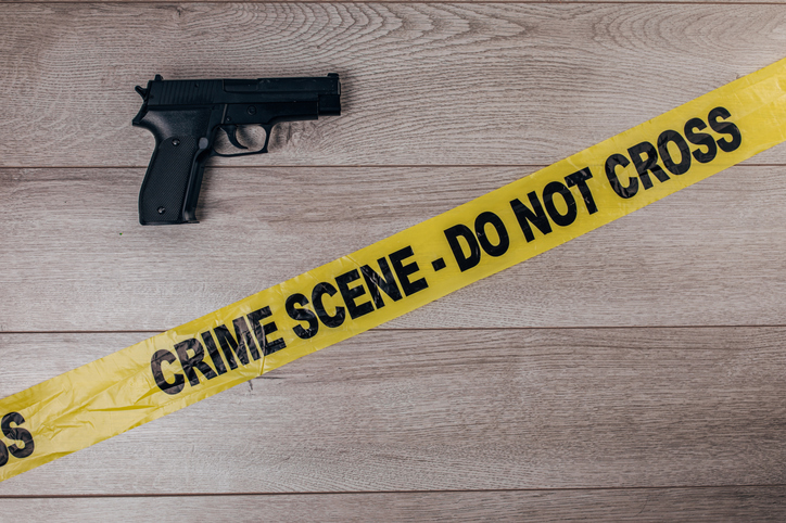 Crime scene tape and gun on wooden background