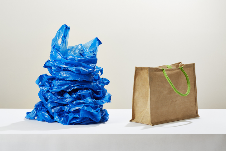A stack of plastic carrier bags next to a reusable shopping bag