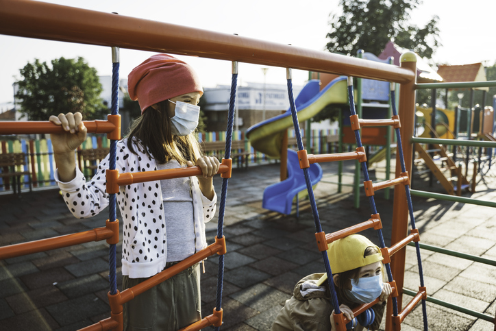 Kids with face protective mask are having fun on the playground. COVID-19, Coronavirus epidemic. New normal. Smiling behind the mask.