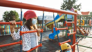 Kids with face protective mask are having fun on the playground. COVID-19, Coronavirus epidemic. New normal. Smiling behind the mask.
