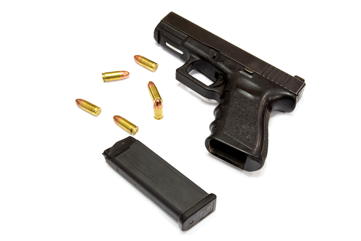 High Angle View Of Hand Gun And Bullets Against White Background