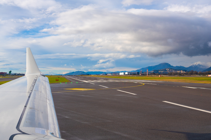 Airplane wing extends over runway with mountains in background on a cloudy day