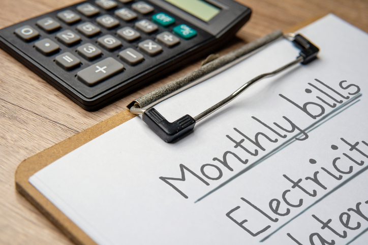 Calculator and a paper clipboard with a handwritten monthly bills list.
