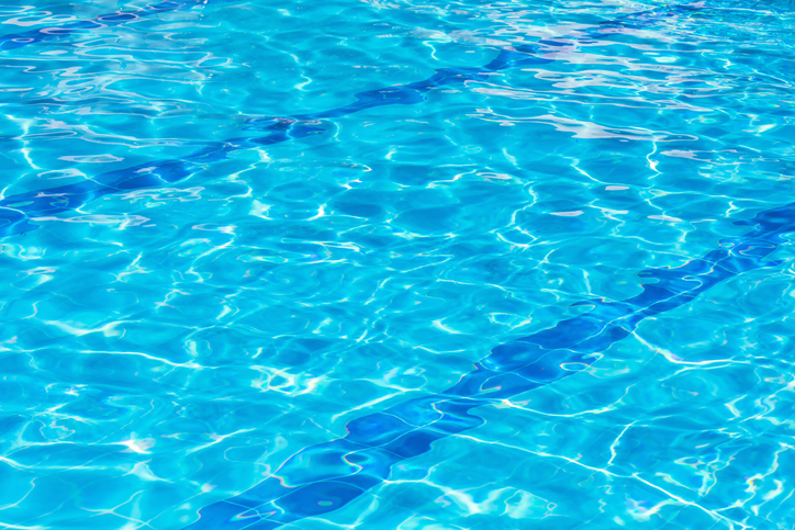 Clear blue swimming pool water surface with sunlight reflections and ripples, perfect summer relaxation background