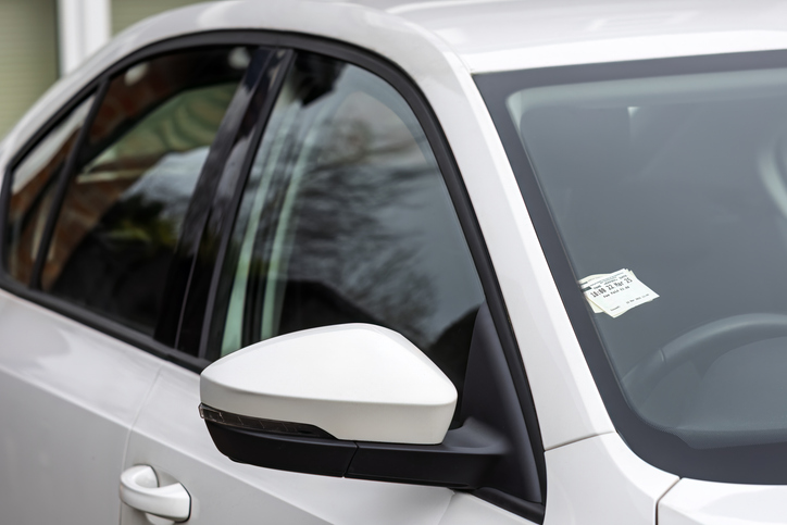 A pay-and-display parking ticket is displayed on the dashboard of a modern white car. The image represents city parking, transportation costs, following rules, and urban life