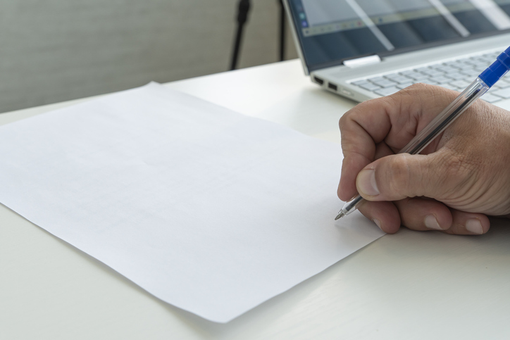 hand with a pen in close-up signs an empty paper document. A man fills a white blank paper form with a pen close-up in bright sunlight.