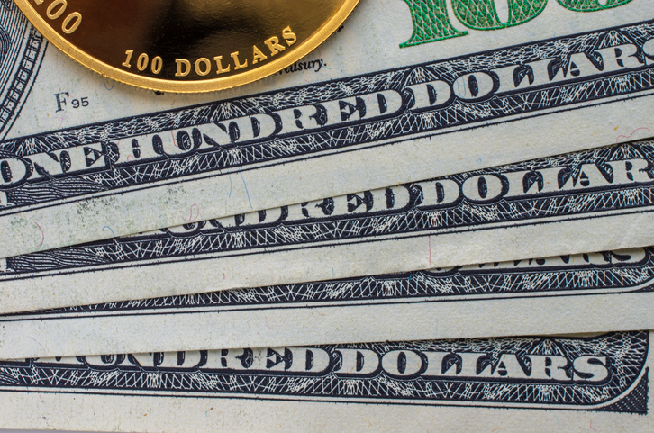 Gold coin with a face value of 100 dollars against the background of a dollar bills