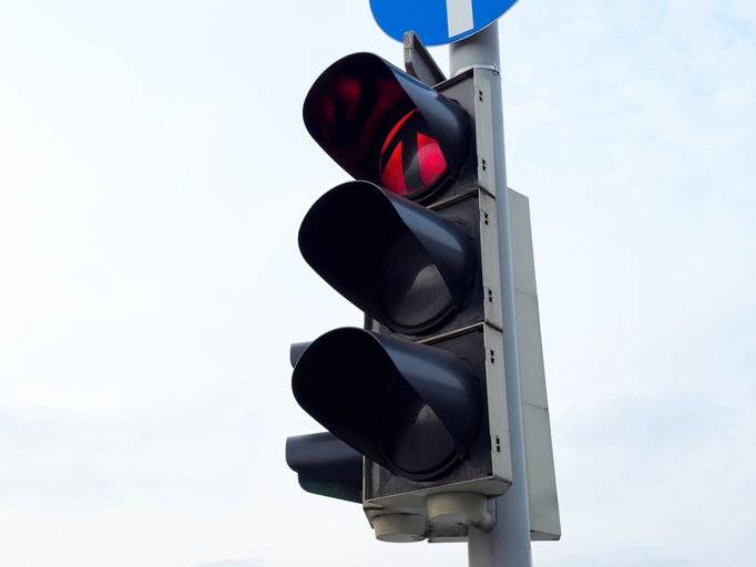 Red traffic light against blue sky in urban setting