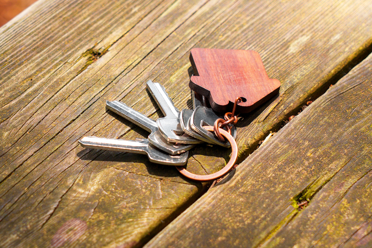 Door keys with house keychain on wooden aged outdoor yard table