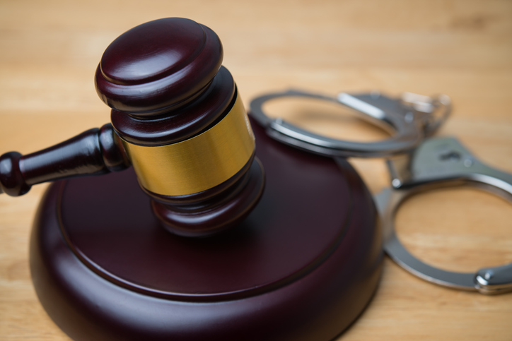 Hammer judge gavel and handcuffs in courtroom on wooden table background.