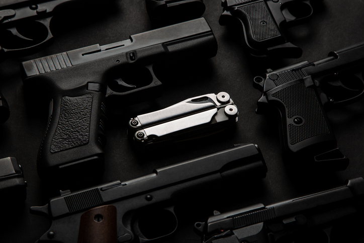 Silver multi-tool among various semi-automatic pistols. Dark background.