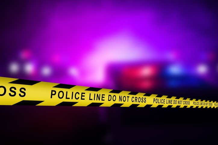 Close Up Shot Focused on Yellow Tape Showing Text "Police Line Do Not Cross". Restricted Area of a Crime Scene. Bokeh Background with Flickering Siren Lights. Forensics Team Working on a Case