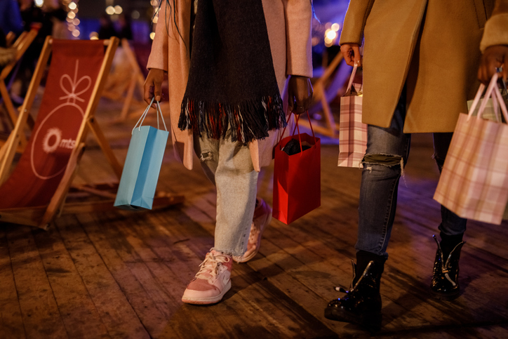 Friends holiday shopping at night, carrying colorful gift bags and stylish outfits on a wooden boardwalk